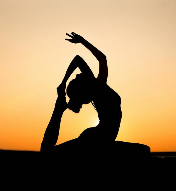 Silhouette of a person in a strong warrior yoga pose at sunset.
